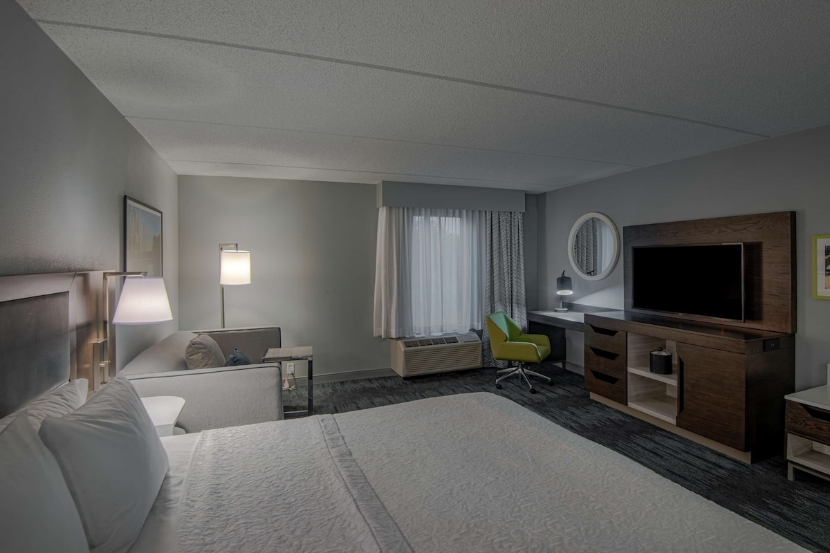 A hotel room with a bed, a desk, a chair, a TV, and a window with curtains.