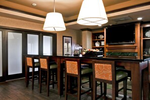 A bar area with wooden bar stools, a television, and a shelf with decorative items. - Hampton Inn Waldorf (Waldorf)