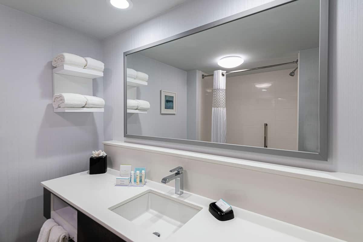 A modern bathroom with a large mirror, white sink, and towel racks.