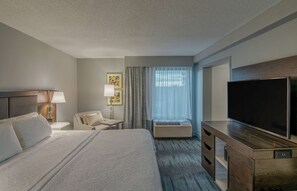 A hotel room with a large bed, a flat-screen TV, a desk with a lamp, a chair, and a window with curtains. - Hampton Inn Waldorf (Waldorf)