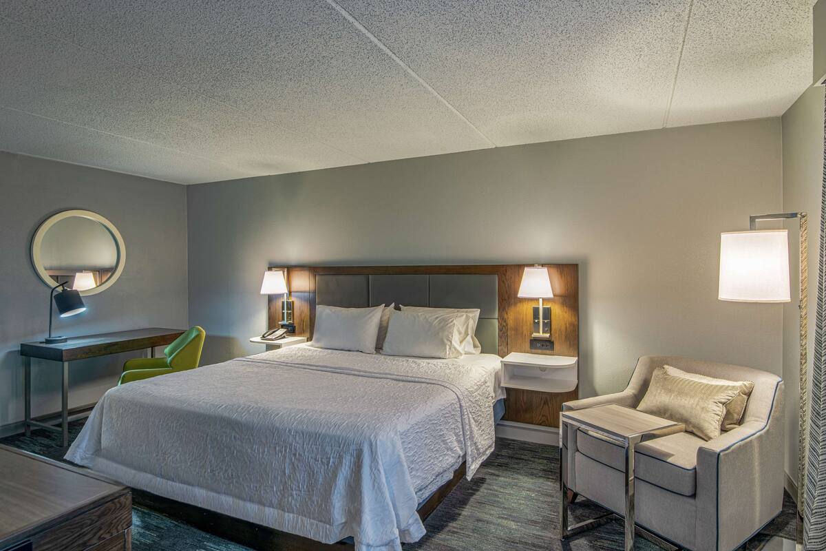 A hotel room with a large bed, a desk, a chair, and a sofa.