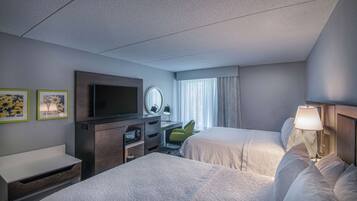A hotel room with two beds, a TV, a desk with a lamp, and a window with curtains.
