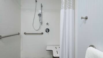 Ein Badezimmer mit weißen Fliesen, einer Dusche inklusive Handbrause, einer Haltestange und einem weißen Waschbecken mit einem Handtuch an der Wand.
