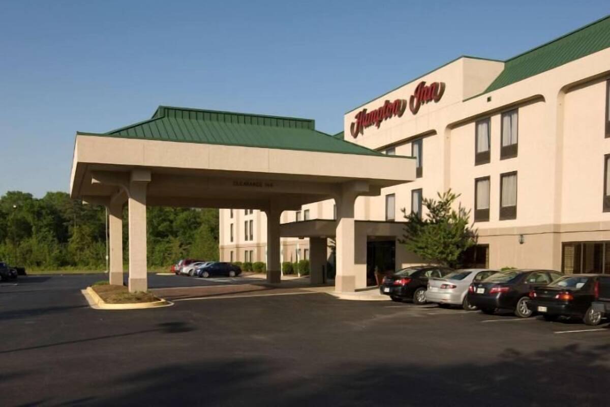 Un hotel Hampton Inn con zona de estacionamiento techada y varios coches aparcados en la parte delantera.