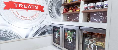 A refrigerated display case with snacks and drinks, and a wall with a circular design and the word 'TREATES'.