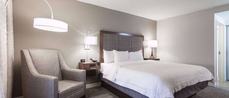 A hotel room with a large bed, a chair, bedside tables, lamps, and a headboard.