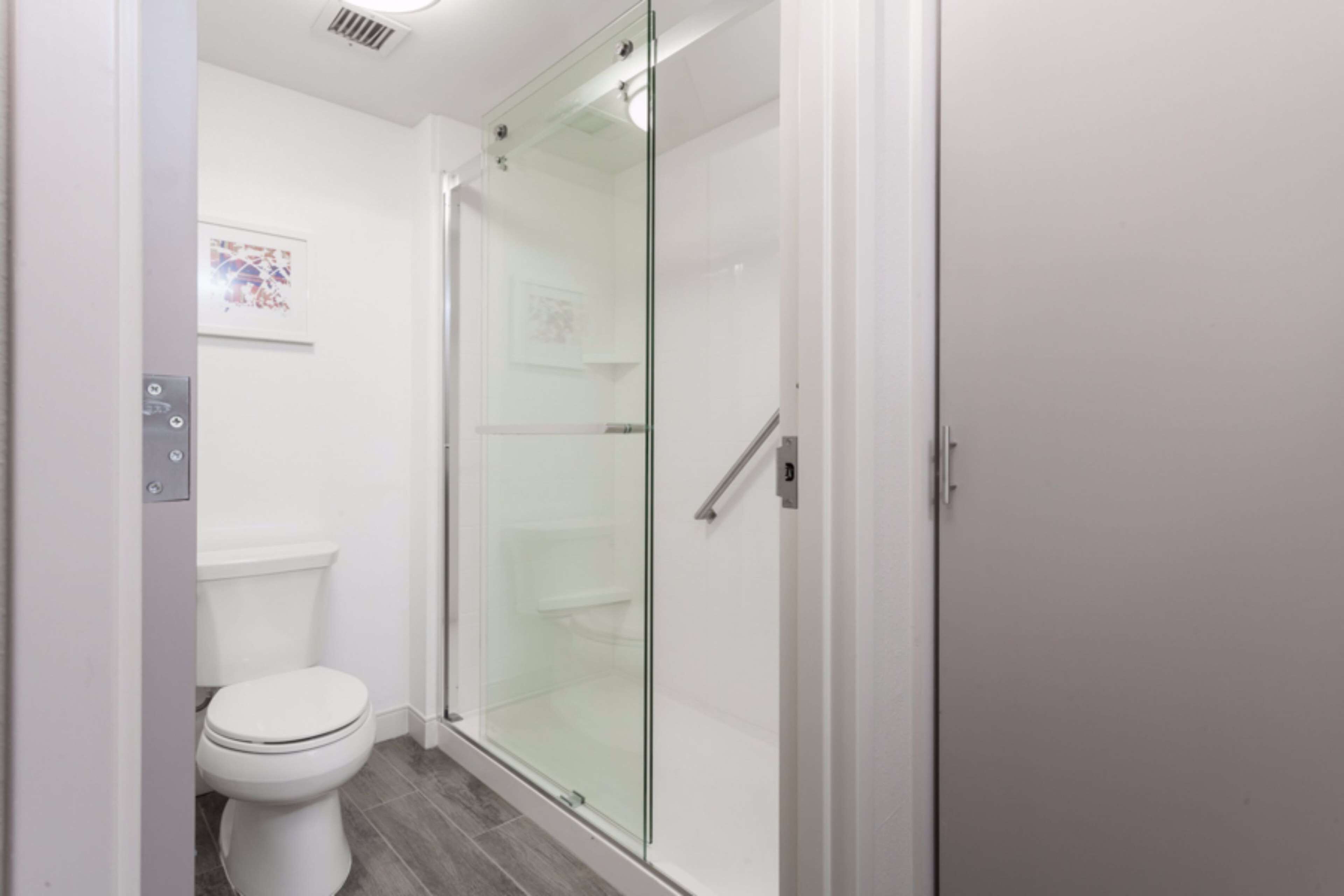 Une salle de bain moderne avec une douche à parois de verre, des toilettes blanches et un sol carrelé.
