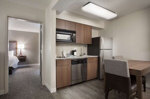 Una cocina de hotel compacta con armarios de madera, electrodomésticos de acero inoxidable y un comedor con mesa y sillas.