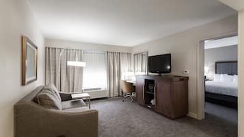 A hotel room with a bed, a desk, a chair, a television, and a window with curtains.