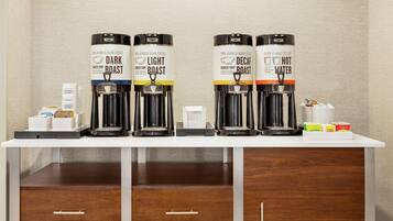 Una estación de café con cuatro dispensadores de café etiquetados como 'Dark Roast', 'Light Roast', 'Decaf' y 'Hot Water'. Hay cápsulas de café y un recipiente pequeño en la encimera.