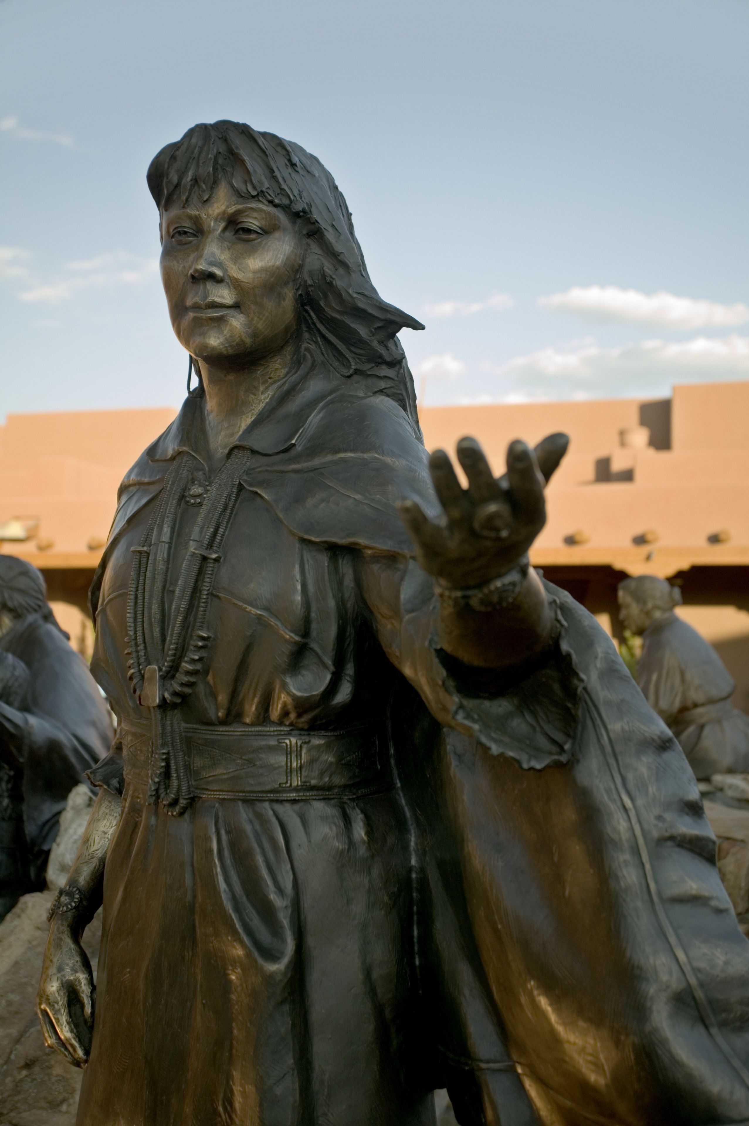A statue of a person with a raised hand, wearing a robe and a belt.