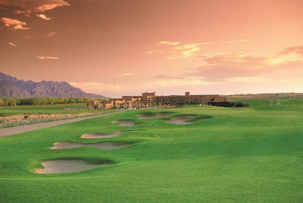 A golf course with bunkers, a clubhouse, and mountains in the background.