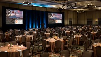 Un amplio salón de banquetes con mesas redondas, sillas y un escenario con una pantalla que muestra el logotipo de Hyatt Regency.