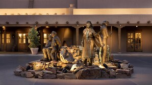 A courtyard with a statue of a Native American figure, a stone wall, and a building with a flat roof and columns. - Hyatt Regency Tamaya Resort & Spa (Santa Ana Pueblo)