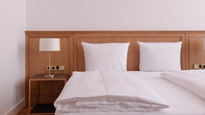 A neatly made bed with white linens, a wooden headboard, and a bedside table with a lamp. - Hotel Lindenufer (Berlin)