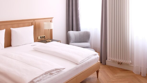 A hotel room with a large bed, a nightstand, a lamp, a chair, and a window with curtains. - Hotel Lindenufer (Berlin)