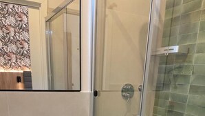 A modern bathroom with a glass shower enclosure, a white sink with toiletries, and a towel rack.