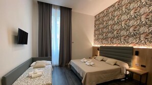 A hotel room with two beds, a TV mounted on the wall, a patterned wallpaper, and a nightstand with a lamp.