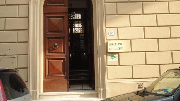 A building entrance with a wooden door and a sign reading "SOCCORSO LE CAMELIE."