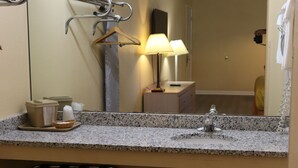 A bathroom with a granite countertop, a sink, a mirror, a towel rack, a lamp, and a trash can. - Woodstream Inn (Hogansville)