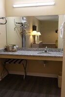 Un baño con encimera de granito, un lavabo, un espejo, toallero, lámpara y cubo de basura.