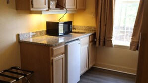 A kitchen with granite countertops, white cabinets, a built-in dishwasher, and a window with curtains. - Woodstream Inn (Hogansville)