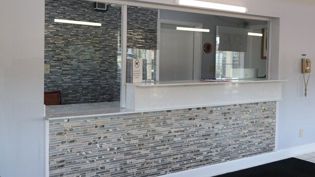 A reception area with a glass partition, a reception desk, and a tiled wall. - Woodstream Inn (Hogansville)