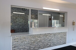 Zona de recepción con separador de vidrio, mostrador de recepción y pared de azulejos.