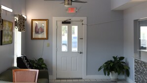 A spacious room with a high ceiling, a large arched window, a ceiling fan, a door with a glass panel, a black rug, a green sofa, a wooden table, and a potted plant. - Woodstream Inn (Hogansville)