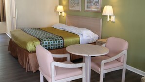 A hotel room with a bed, two chairs, a small table, and two wall-mounted lamps. - Woodstream Inn (Hogansville)