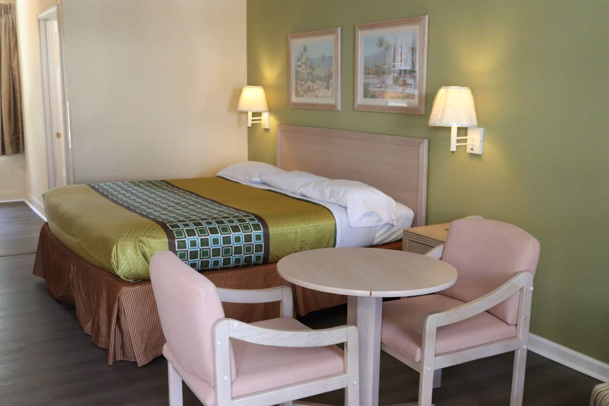 Ett hotellrum med en säng, två stolar, ett litet bord och två vägglampor.