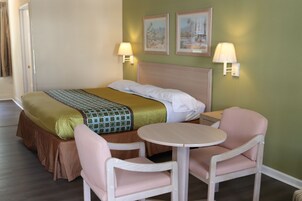 Una habitación de hotel con una cama, dos sillas, una mesita y dos lámparas de pared.