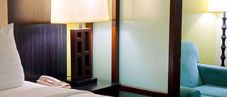 A hotel room with a bed, a nightstand with a lamp, a telephone, and a chair.