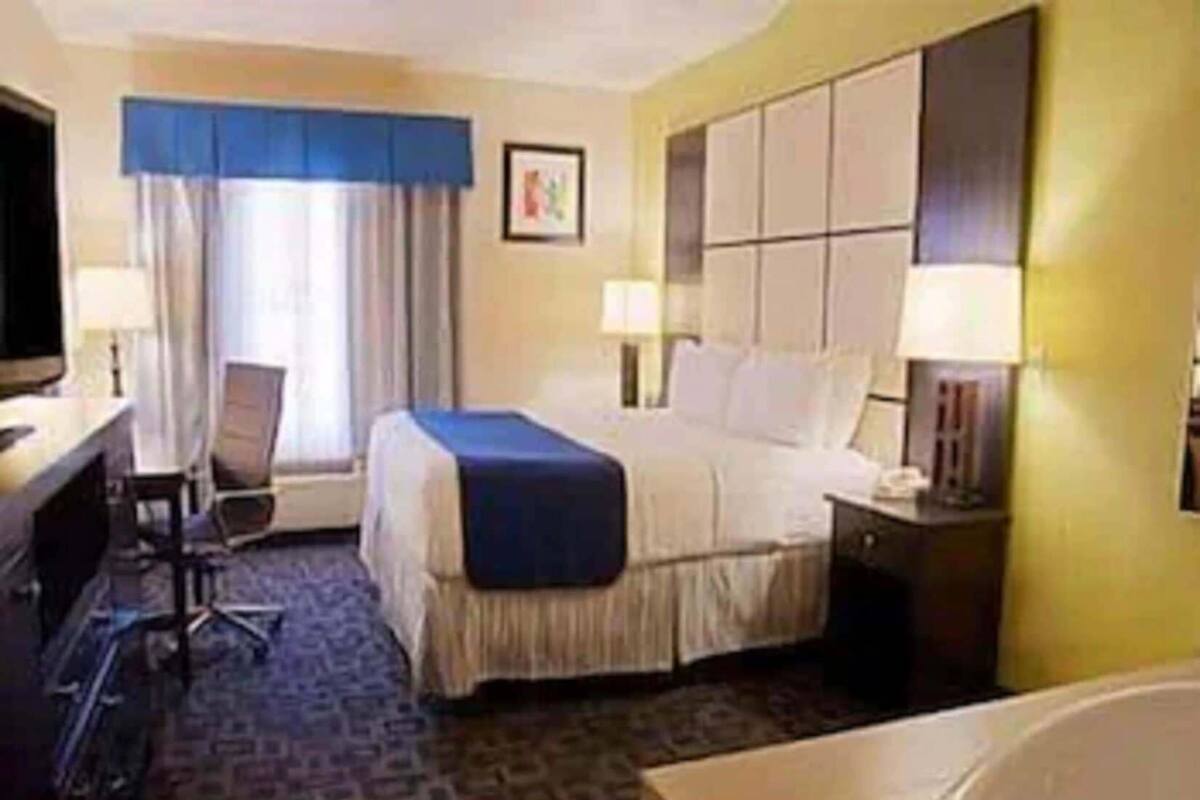 A hotel room with a bed, desk, chair, and a large window with curtains.