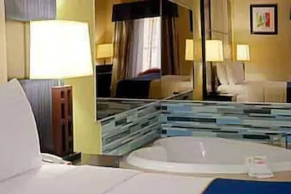 A hotel room with a bed, a bathroom with a bathtub, and a mirror reflecting the room.