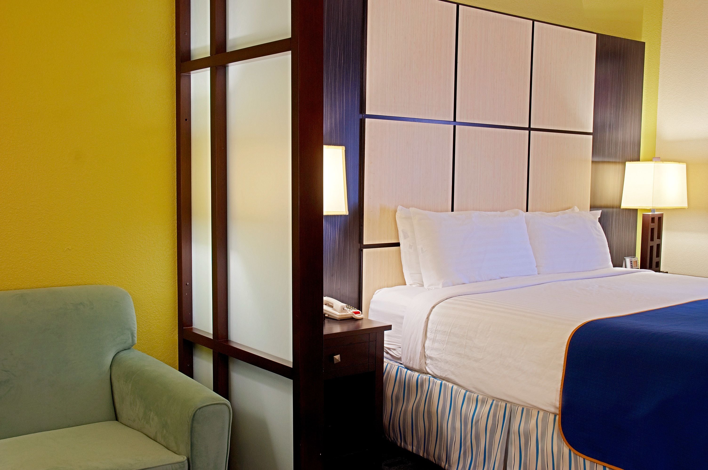 Habitación de hotel con cama, mesita de noche con lámpara, una silla y un teléfono sobre la mesa.