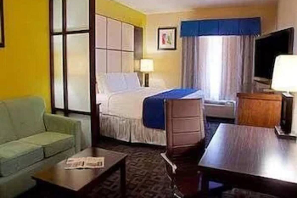 A hotel room with a bed, a desk, a chair, a TV, and a window with curtains.