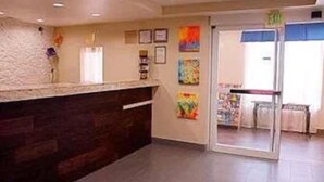 A reception area with a counter, framed artwork on the wall, and a glass door leading to another room. - Super 8 by Wyndham Irving/DFW Apt/North (Irving)