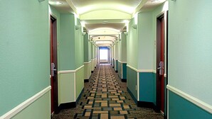 A hotel hallway with a patterned carpet, teal walls, and doors on both sides. - Super 8 by Wyndham Irving/DFW Apt/North (Irving)