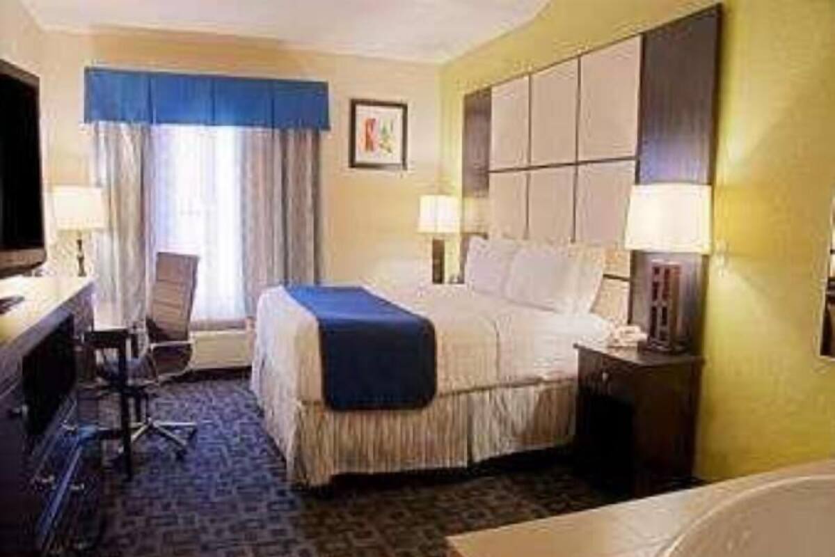 A hotel room with a bed, a desk with a chair, a television, and a window with curtains.
