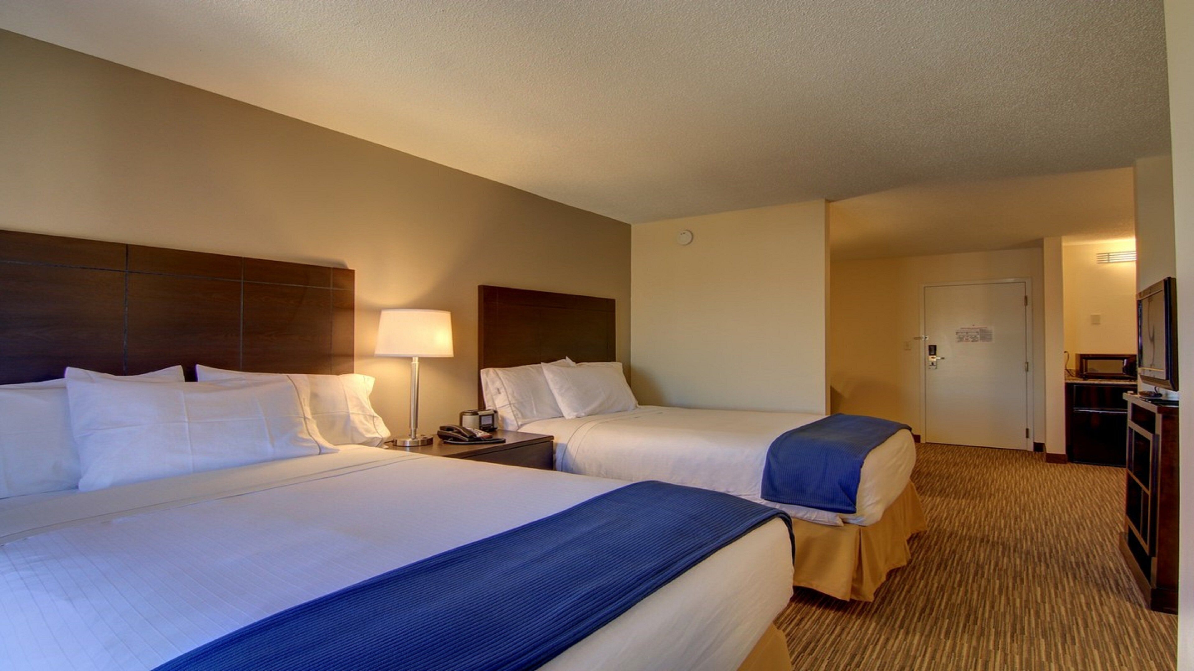 A hotel room with two beds, a desk, a lamp, and a television.