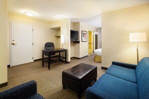 A hotel room with a sofa, a small table with a chair, a television, and a lamp. - Holiday Inn Express & Suites Alpharetta - Windward Parkway by IHG (Alpharetta)