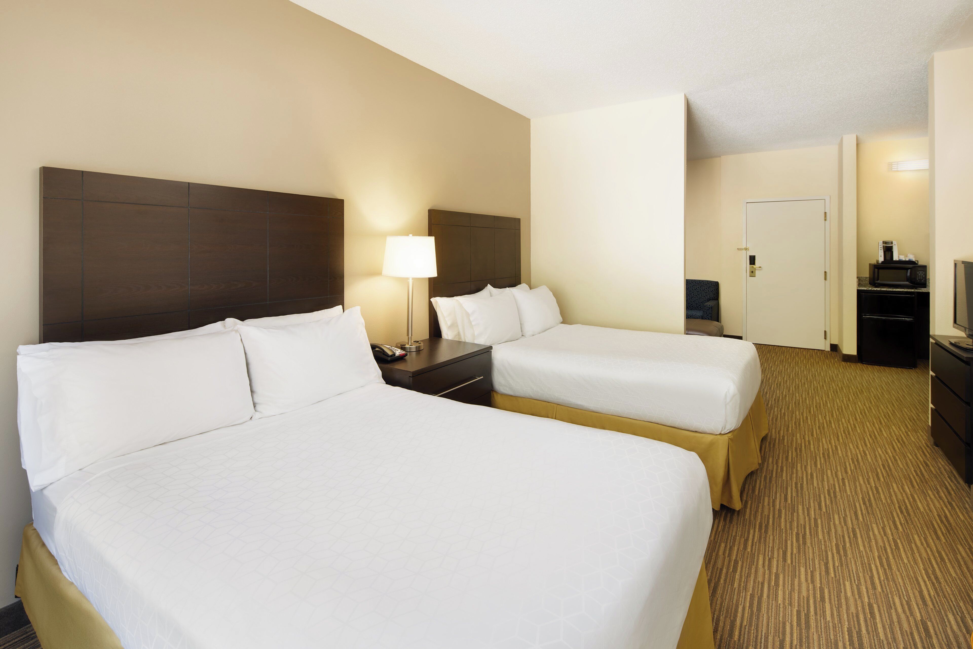 Habitación de hotel con dos camas, un escritorio, una lámpara, un teléfono, un microondas y una televisión.