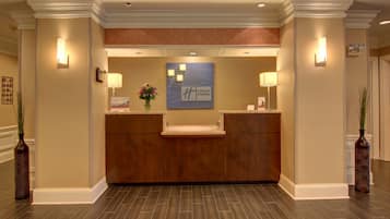 Een hotel receptie met een houten receptiebalie, een blauw bord met het 'Holiday Inn Express' logo, en twee wandlampen.