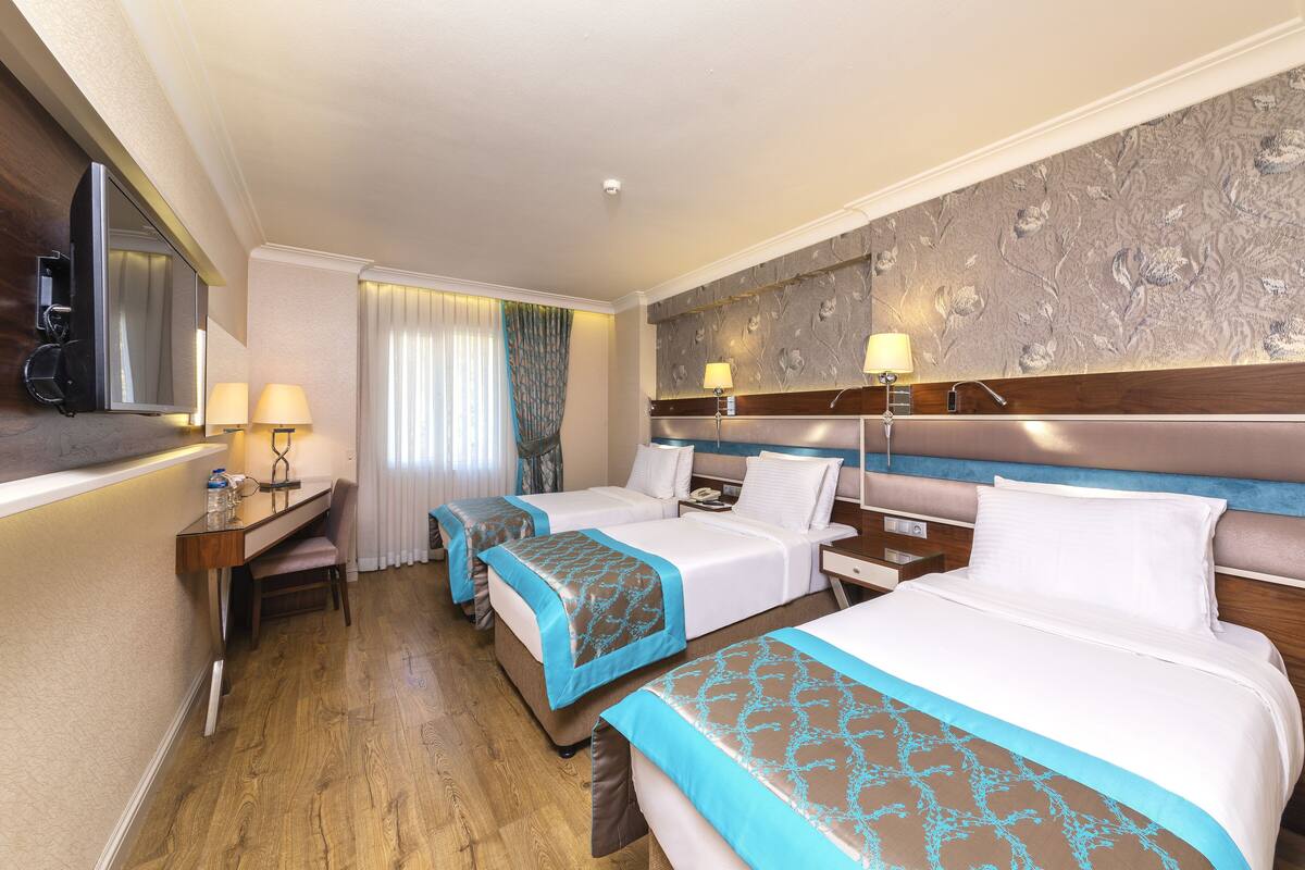 A hotel room with two beds, a desk with a chair, a mirror, and a window with curtains.