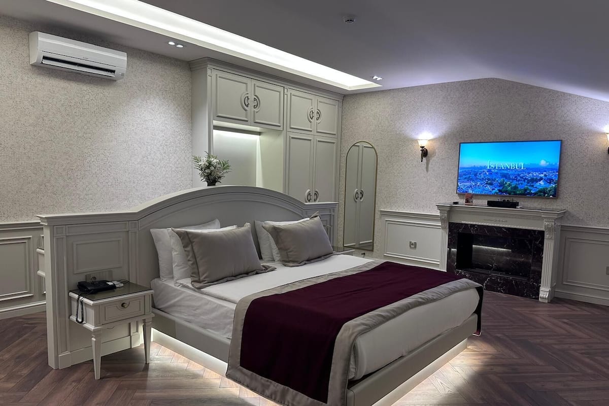 A modern bedroom with a large bed, a TV, and a fireplace.