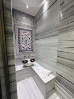 A modern bathroom with a marble vanity, a large decorative tile above the sink, and a towel rack.