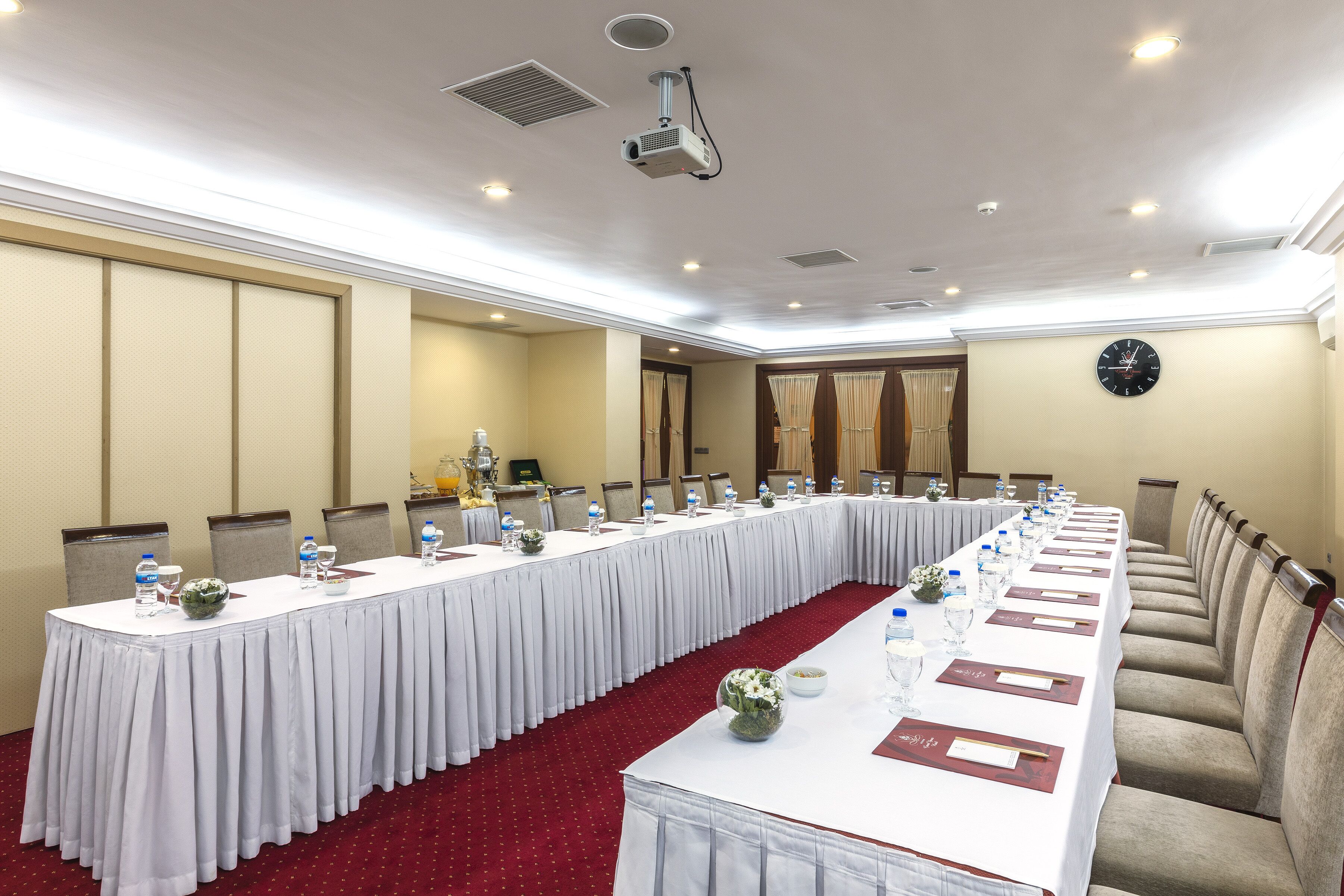 A conference room with a long table, chairs, water bottles, and a clock on the wall.