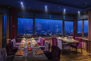 Zona pranzo con vista sulla città, ampie finestre e poltrone rivestite in viola.