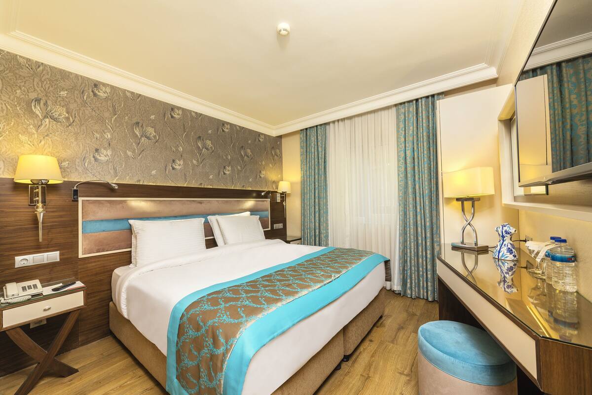 A hotel room with a large bed, a desk with a lamp, a mirror, and a bathroom area.